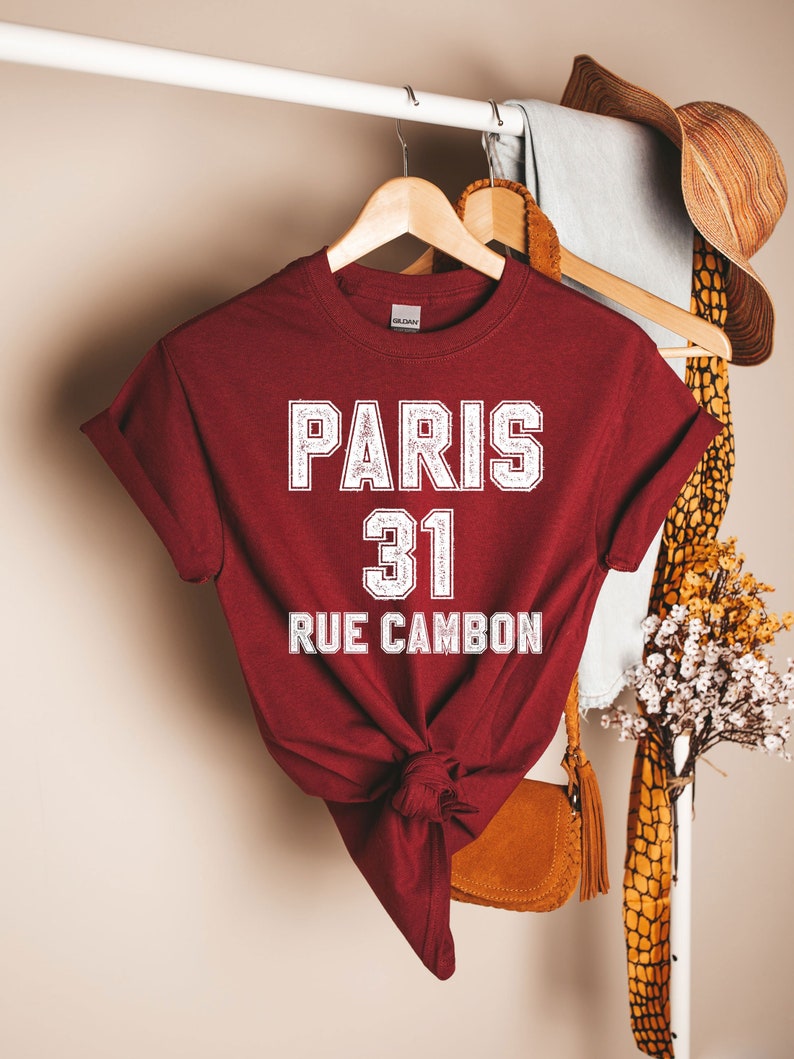 Pu&ograve; includere: Una maglietta color granata con testo bianco che recita "PARIS 31 RUE CAMBON".