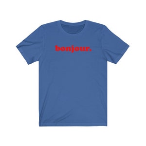 Pode incluir: Uma camiseta azul royal com a palavra "bonjour" impressa em vermelho.