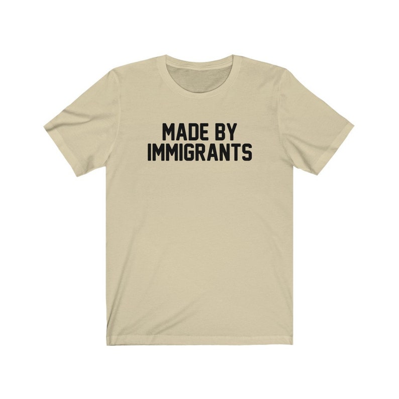 May include: A beige t-shirt with the text "MADE BY IMMIGRANTS" printed in black.
