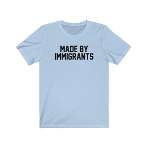 May include: Light blue t-shirt with the text "MADE BY IMMIGRANTS" printed in black.