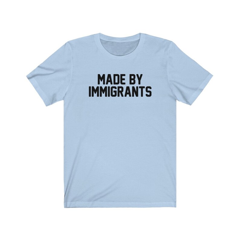 May include: Light blue t-shirt with the text "MADE BY IMMIGRANTS" printed in black.