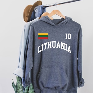 May include: A dark gray hoodie with the word "LITHUANIA" in white arched lettering. The number "10" is printed in white on the right side. The Lithuanian flag is on the left chest. The hoodie has a front pocket and a hood.