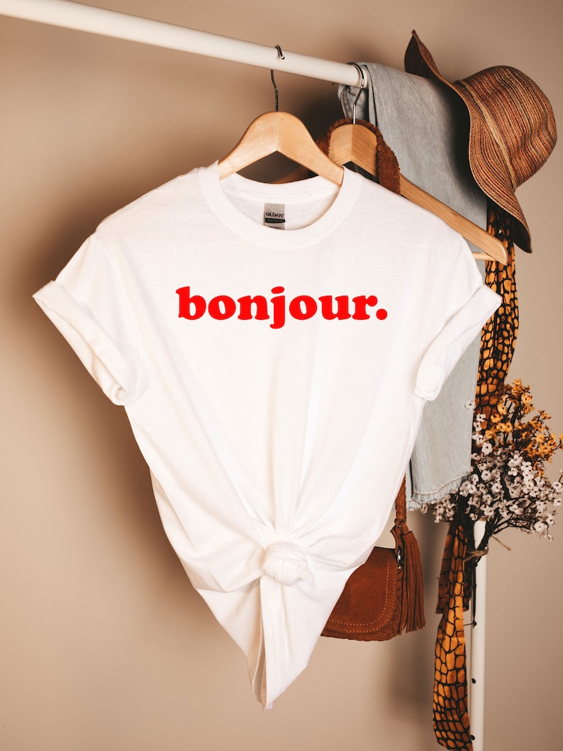 Pode incluir: Camiseta branca com um gr&aacute;fico vermelho "bonjour".