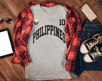 May include: A gray t-shirt with a black graphic of the word "PHILIPPINES" in an arc with a number "10" above it. The graphic also includes a small emblem with the colors of the Philippine flag.