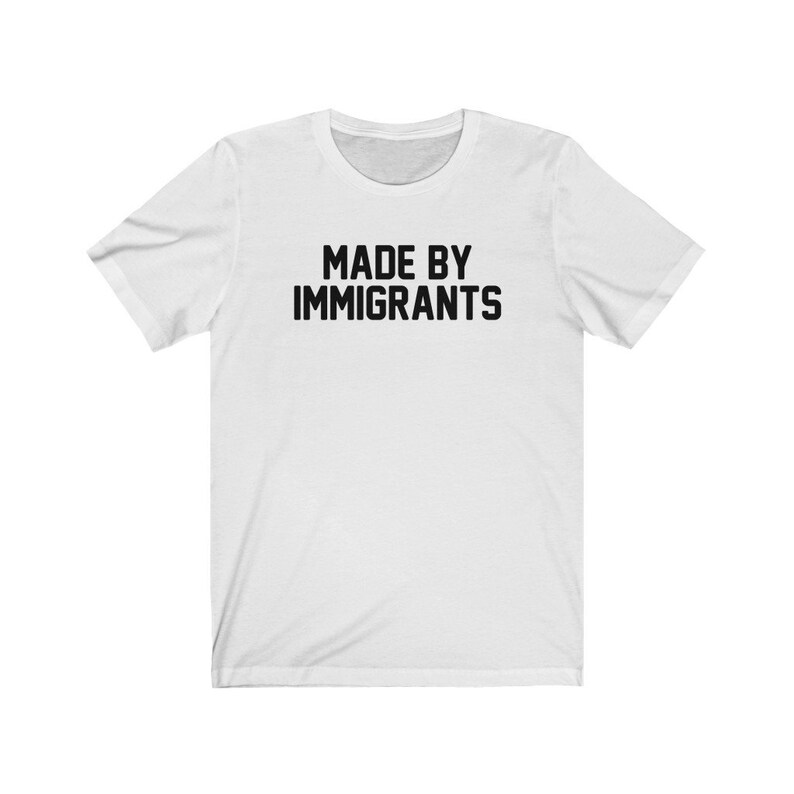 May include: White t-shirt with black text that reads "MADE BY IMMIGRANTS".