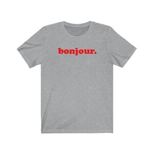 Pode incluir: Uma camiseta cinza mescla com a palavra "bonjour" impressa em vermelho.