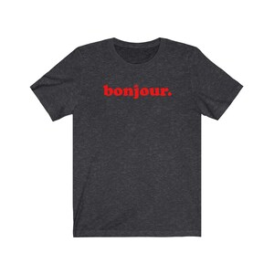 Pode incluir: Uma camiseta cinza escura com a palavra "bonjour" impressa em vermelho.