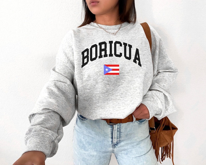May include: A gray sweatshirt with the word "BORICUA" in black letters and the Puerto Rican flag printed on the front.