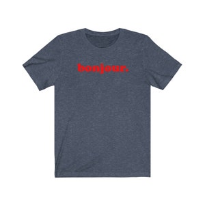 Pode incluir: Uma camiseta azul escura com a palavra "bonjour" impressa em vermelho na frente.