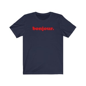 Pode incluir: Uma camiseta azul marinho com a palavra "bonjour" impressa em vermelho na frente.