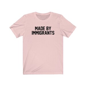 May include: A pink t-shirt with the text "MADE BY IMMIGRANTS" printed in black.