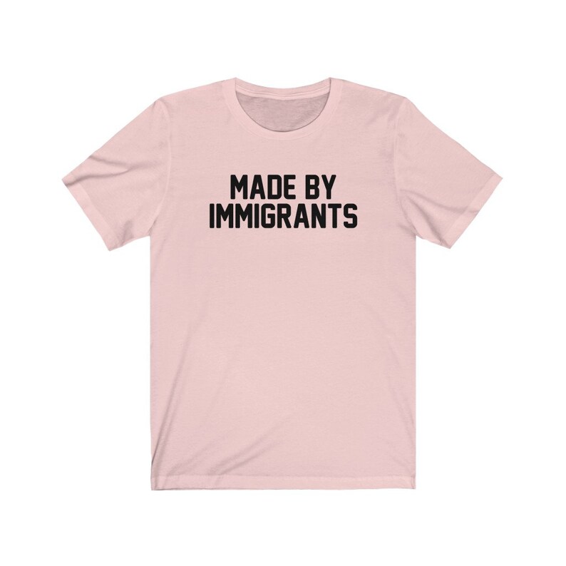 May include: A pink t-shirt with the text "MADE BY IMMIGRANTS" printed in black.