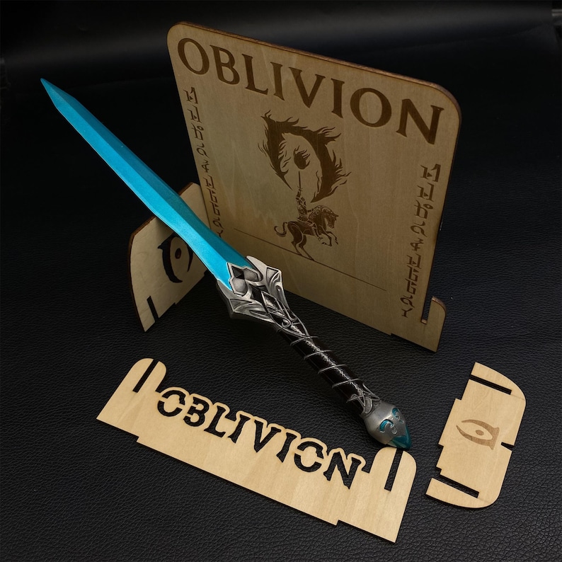 May include: A fantasy-themed wooden display featuring a blue and silver sword with a black handle. The display includes a wooden stand with the word "OBLIVION" and a logo. The sword has a blue blade and intricate silver detailing.