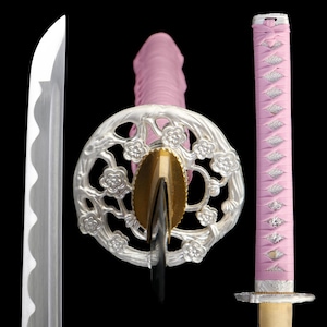 Op de afbeelding: Een gedetailleerd beeld van een katana-zwaard. Het lemmet is zilverkleurig en de handgreep is gewikkeld in roze stof. De pareerstang is zilverkleurig met een bloemmotief en de pommel is goudkleurig. Het zwaard staat tegen een zwarte achtergrond.