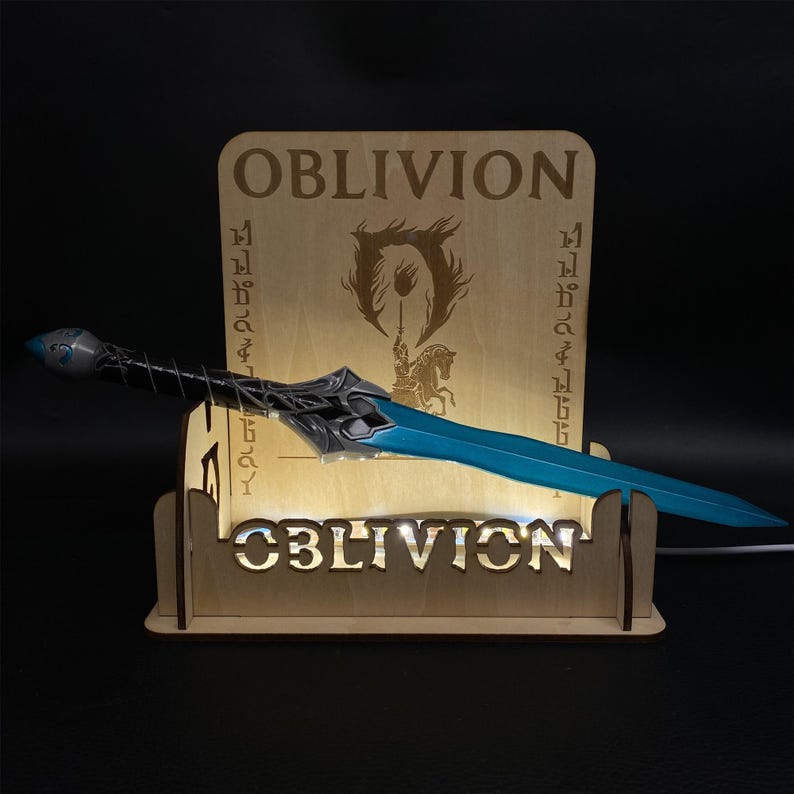 May include: A blue and silver fantasy sword rests on a wooden display stand. The stand is illuminated and features the word "OBLIVION" and the game's logo. The sword has a detailed hilt and a bright blue blade.