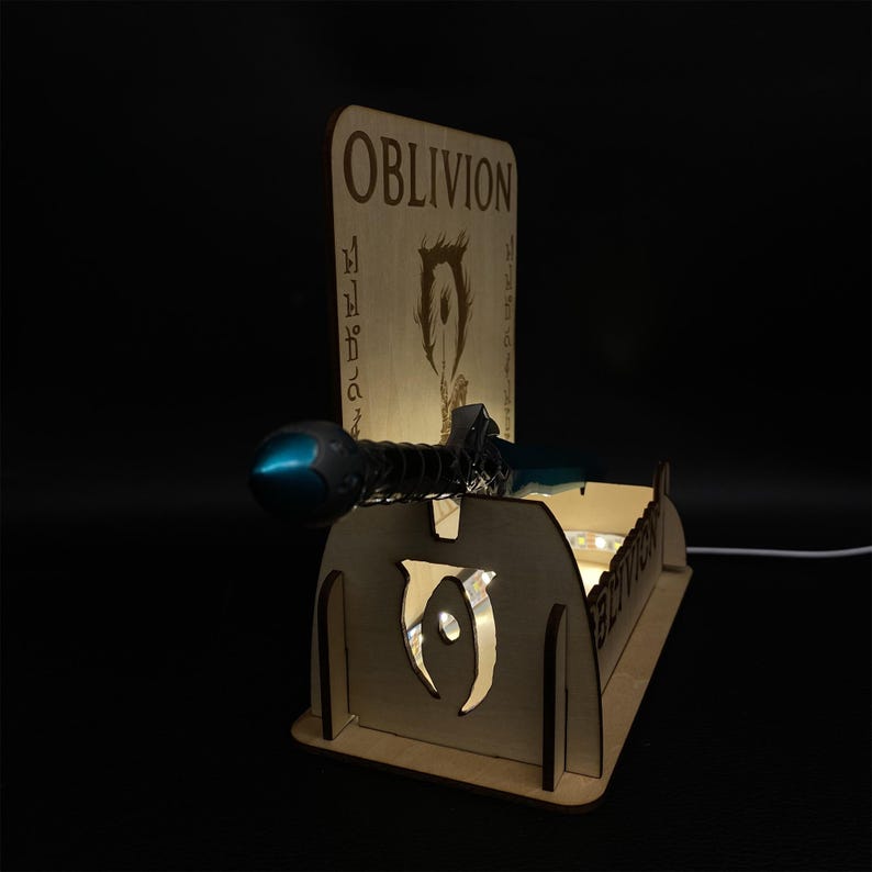 May include: A wooden display stand with the word "OBLIVION" engraved on the back. The stand features a sword and a glowing light. The stand is made of light brown wood and has a cutout design on the front.