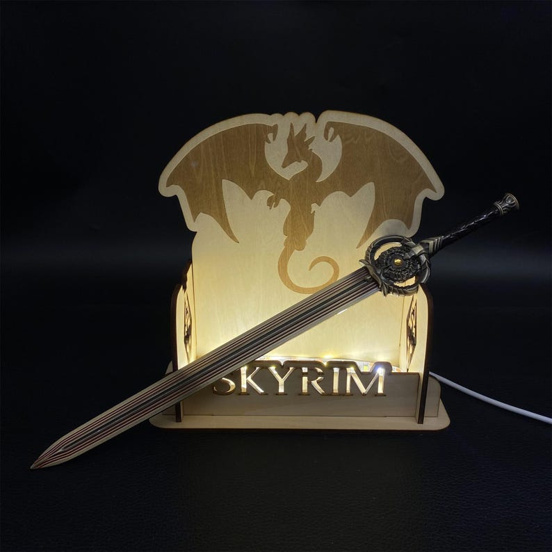 May include: A decorative wooden light-up display featuring a sword and the word "SKYRIM". The sword has a detailed hilt and blade. The display has a dragon silhouette and small lights.