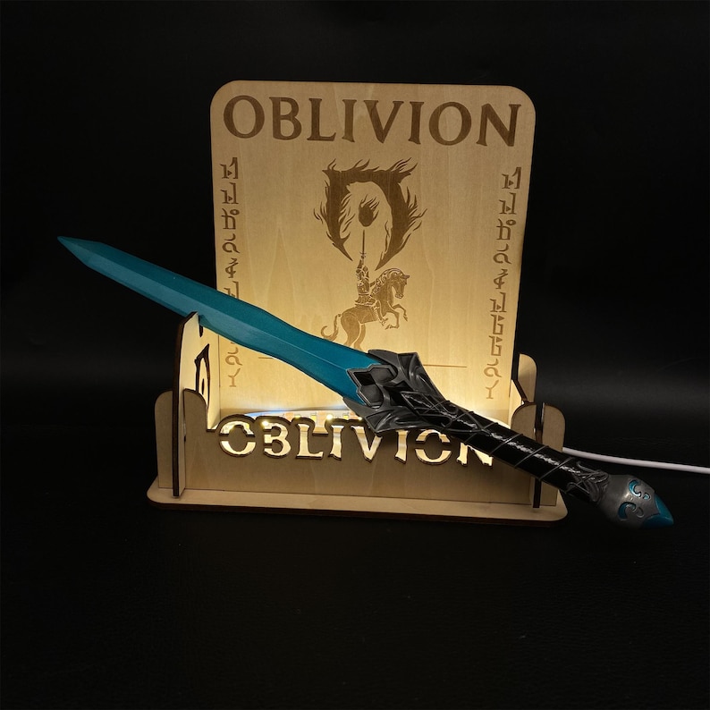 May include: A wooden display featuring the word "OBLIVION" and a stylized image of a knight on a horse. A blue and silver sword is positioned in front of the display. The word "OBLIVION" is also displayed on the base.