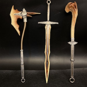May include: Three fantasy weapons: an axe, a sword, and a dagger. The axe has a wooden head and a silver handle. The sword has a silver hilt and a gold blade. The dagger has a bone handle and a silver blade. All three weapons are displayed against a dark background.