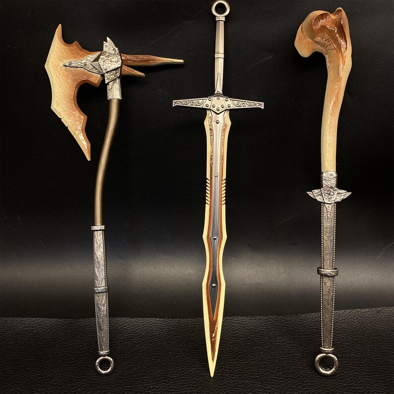 May include: Three fantasy weapons: an axe, a sword, and a dagger. The axe has a wooden head and a silver handle. The sword has a silver hilt and a gold blade. The dagger has a bone handle and a silver blade. All three weapons are displayed against a dark background.