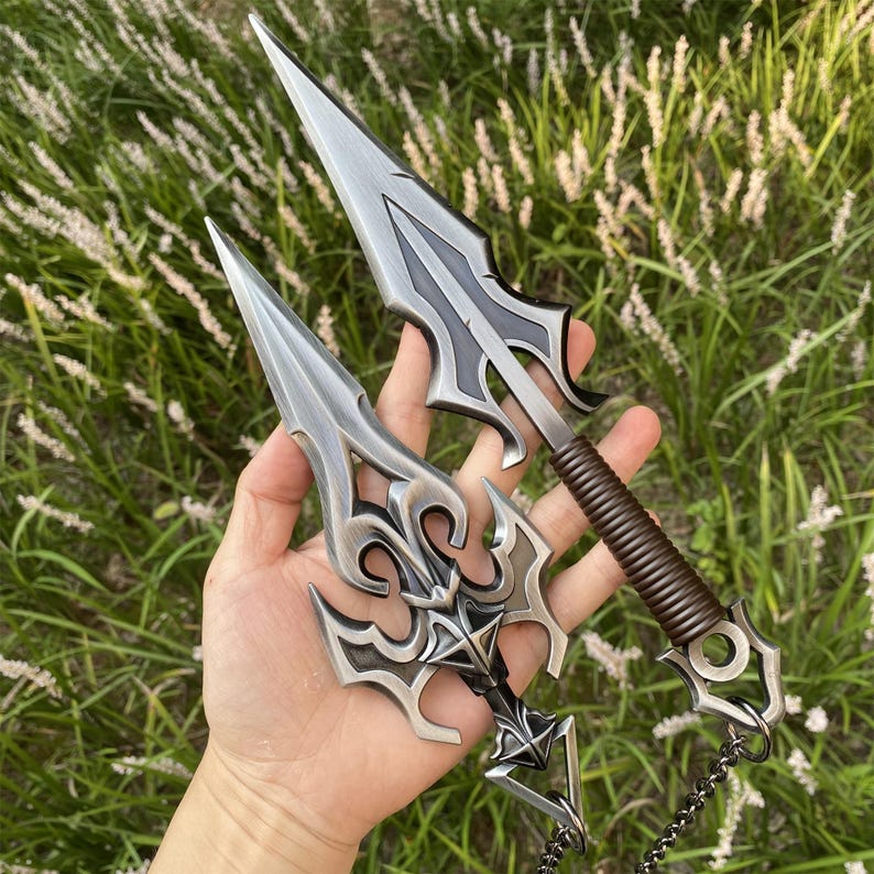 May include: Two decorative daggers with silver blades and ornate black and silver handles. One dagger has a wrapped brown handle. The daggers have a pointed tip and a decorative design on the handle.