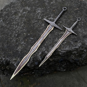 May include: Two decorative swords with ornate designs. The blades have a light brown center with a dark brown edge and a silver-colored spine. The hilts and crossguards are dark gray with decorative patterns. One sword is larger than the other.