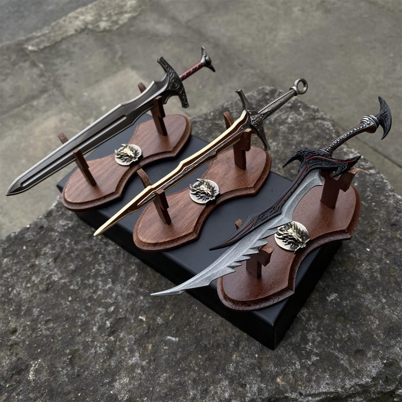 May include: Three decorative swords on wooden plaques. The swords have intricate designs and are displayed on dark wooden stands. Each plaque features a metal emblem. The swords vary in color, including silver, gold, and black.