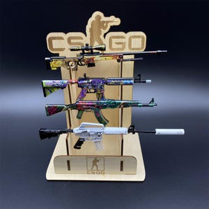 Puede incluir: Un expositor de madera con cuatro rifles de juguete con dise&ntilde;os florales y geom&eacute;tricos coloridos. El expositor tiene el texto "CS GO" y una silueta de un tirador. Los rifles son de varios tama&ntilde;os y estilos.