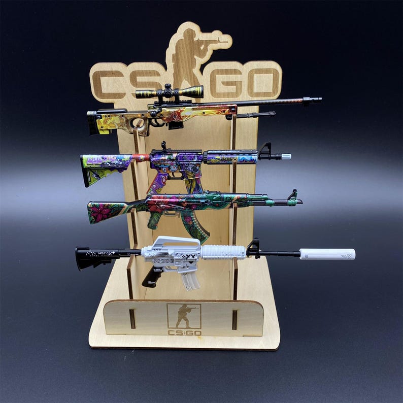 Puede incluir: Un expositor de madera con cuatro rifles de juguete con dise&ntilde;os florales y geom&eacute;tricos coloridos. El expositor tiene el texto "CS GO" y una silueta de un tirador. Los rifles son de varios tama&ntilde;os y estilos.