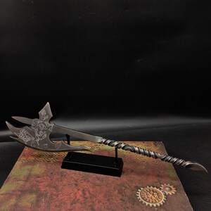 May include: A silver-colored decorative axe with intricate designs on the blade, mounted on a black stand. The axe has a twisted handle and a sharp point.