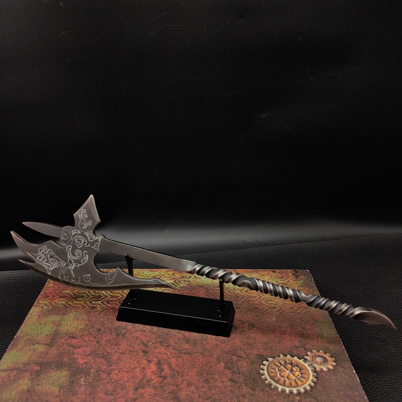 May include: A silver-colored decorative axe with intricate designs on the blade, mounted on a black stand. The axe has a twisted handle and a sharp point.