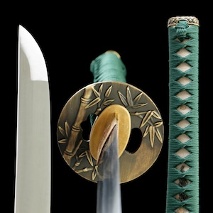 May include: A Japanese katana sword with a polished silver blade. The guard is bronze with a bamboo design, and the handle is wrapped in green fabric. The sword's components are displayed against a black background.