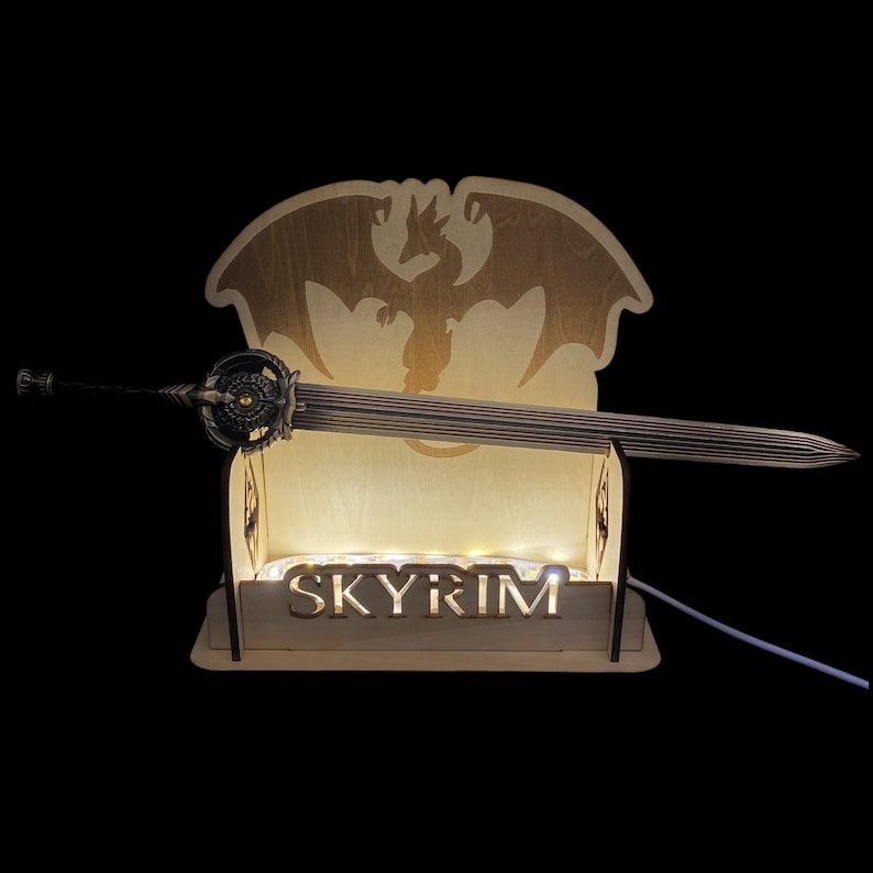 May include: A wooden display stand with the word "SKYRIM" illuminated at the base, holding a detailed sword. The stand features a dragon silhouette and small lights. The sword has an ornate hilt and a ribbed blade.