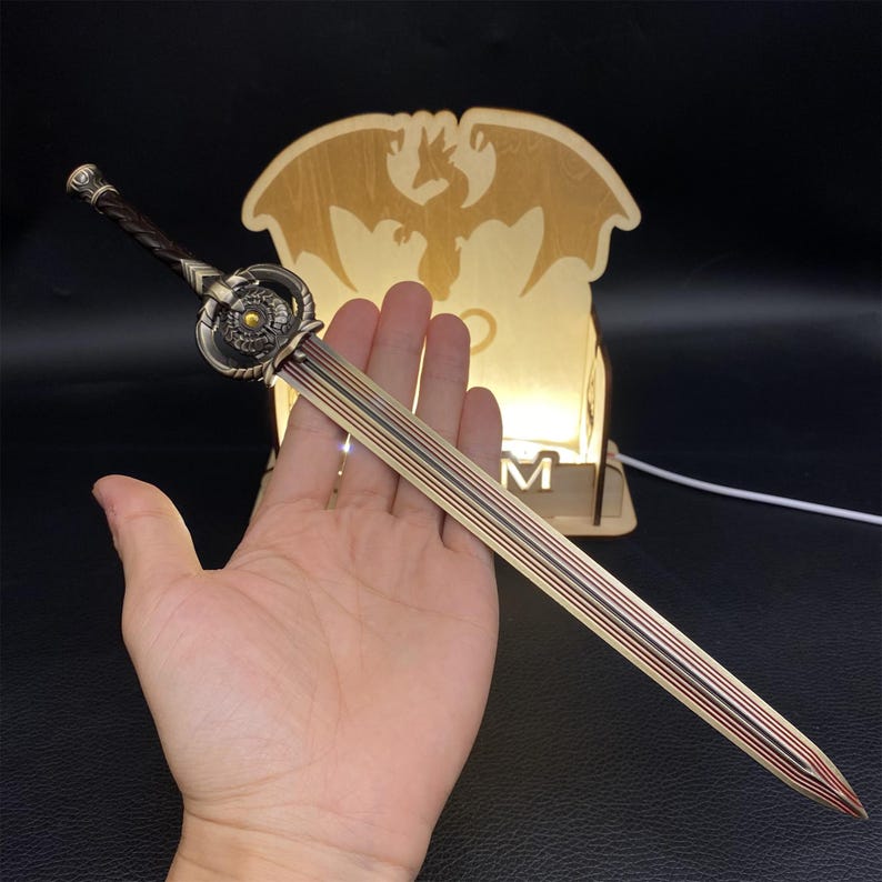 May include: A decorative sword with a bronze blade and a detailed hilt. The handle is wrapped in a dark brown material. The sword is held in a hand, with a wooden dragon-shaped light in the background.
