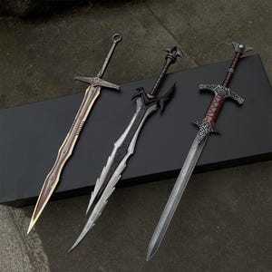 May include: Three fantasy swords with ornate designs. The swords have silver, gold, and black blades with detailed hilts. The blades are approximately 30 inches long. The swords are displayed on a black surface.