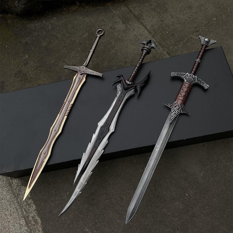 May include: Three fantasy swords with ornate designs. The swords have silver, gold, and black blades with detailed hilts. The blades are approximately 30 inches long. The swords are displayed on a black surface.