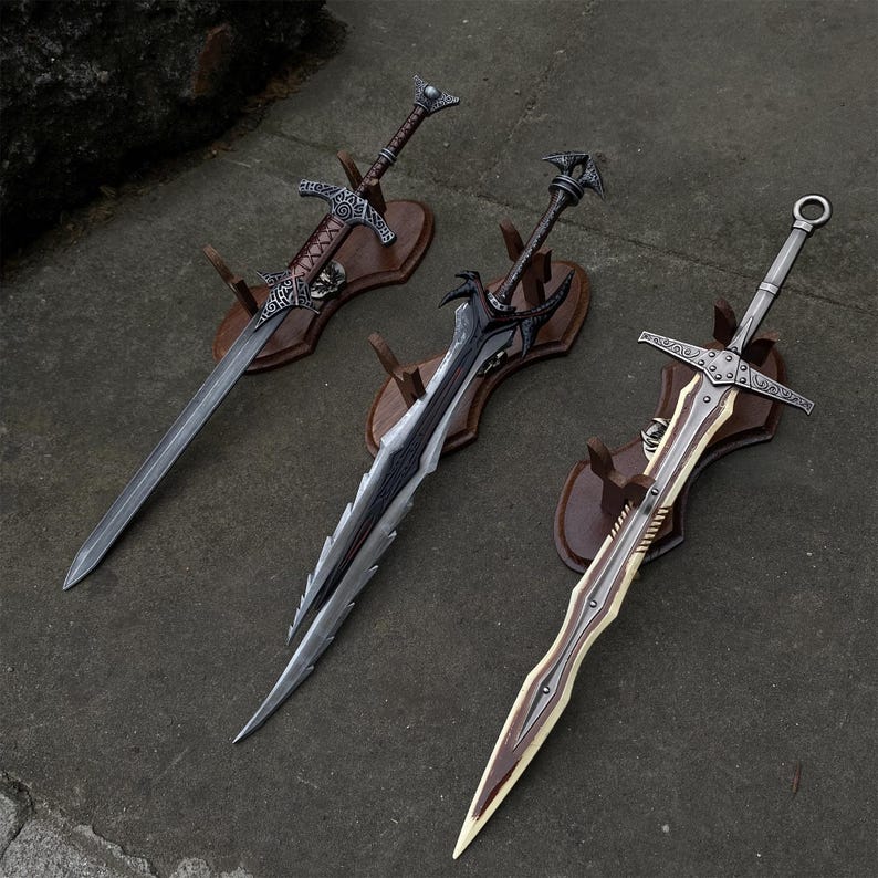 May include: Three decorative swords with ornate designs are displayed on wooden plaques. The swords feature silver blades and detailed handles. One sword has a brown handle, another has a black handle, and the third has a silver handle with a circular pommel.