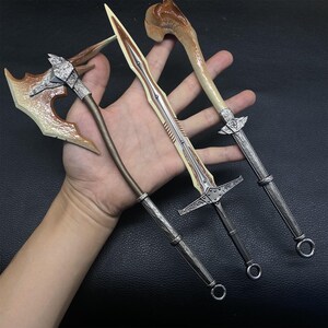 May include: Three miniature fantasy weapons: an axe, a sword, and a mace. The axe has a brown blade and silver accents. The sword has a cream-colored blade and silver hilt. The mace has a bone-colored head and silver handle.