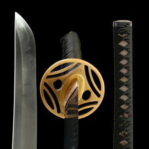 May include: A close-up of a Japanese katana sword. The blade is silver, the guard is gold, and the handle is black with a diamond pattern. The sword is set against a black background.