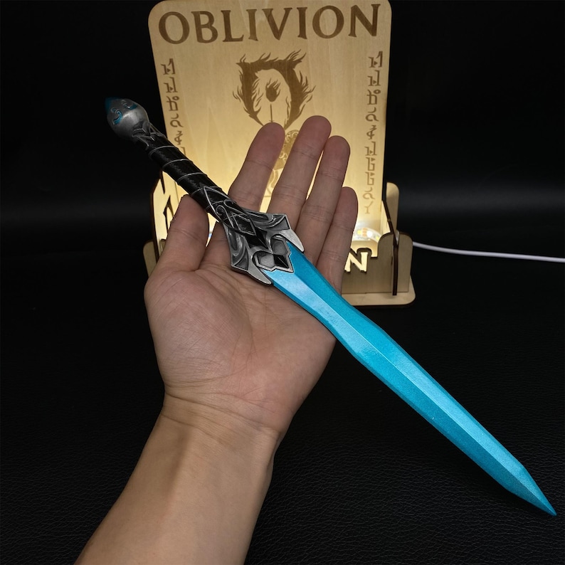 May include: A fantasy-style sword with a light blue blade and ornate silver and black hilt. The sword is held in a hand, with a wooden sign in the background that reads "OBLIVION".