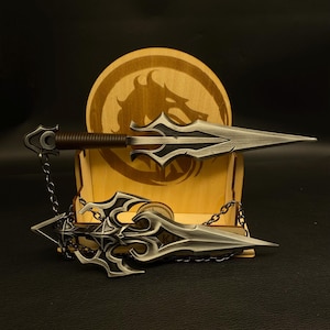 May include: Two decorative daggers with ornate silver blades and dark accents. One dagger has a brown handle and a chain. The daggers are displayed in front of a wooden stand with a dragon emblem.