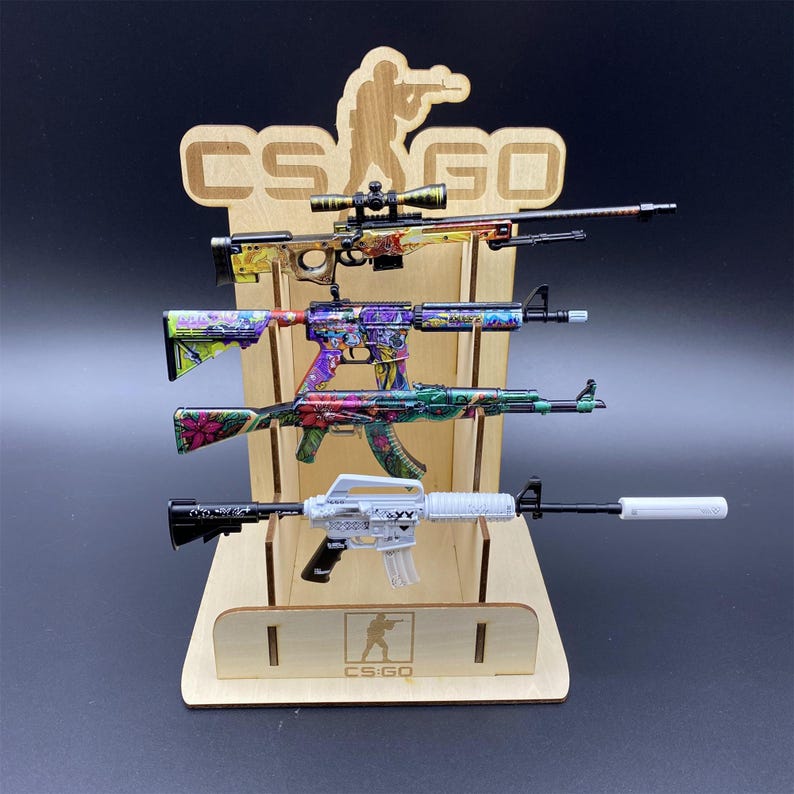 Puede incluir: Un expositor de madera con cuatro armas de juguete con dise&ntilde;os coloridos. El expositor tiene el texto "CS:GO" y una silueta de un tirador. Las armas de juguete tienen varios patrones.