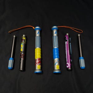 May include: A collection of six screwdrivers with various designs. Two have yellow and blue handles, two have black handles, and one has a purple handle. Each screwdriver has a blue tip and a lanyard.