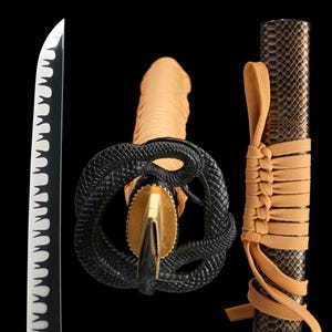 Peut inclure: Gros plan sur un katana. La lame noire a un bord blanc. Le manche est enveloppé de tissu beige, et la garde est un serpent noir au design complexe. Le fourreau est sombre avec un motif peau de serpent, et une corde beige l'entoure.
