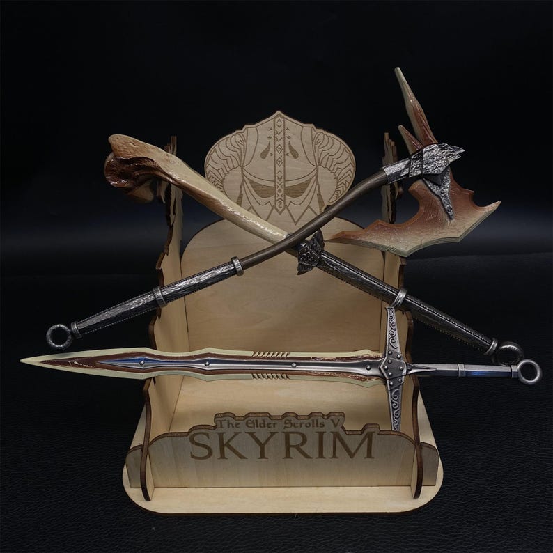 May include: A wooden display stand featuring crossed fantasy weapons from The Elder Scrolls V: Skyrim. The stand holds a bone club, a battle axe, and a sword. The stand is engraved with the game's title.