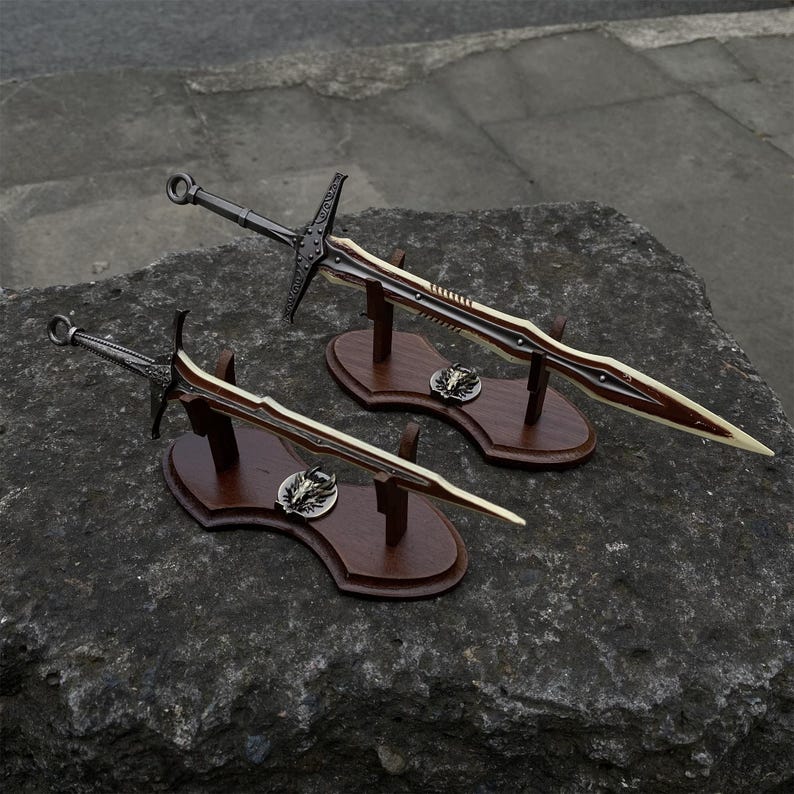 May include: Two decorative swords with brown and cream-colored blades are displayed on wooden stands. The swords have dark metal hilts and crossguards. Each stand features a decorative emblem and is set against a dark, textured background.