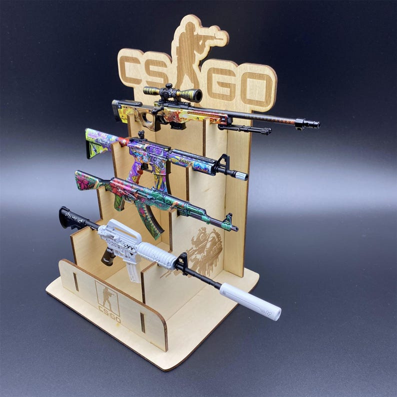 Puede incluir: Un expositor de madera con cuatro pistolas de juguete con dise&ntilde;os coloridos. El expositor tiene el texto "CS GO" y una silueta de una persona apuntando con un arma. Las pistolas est&aacute;n pintadas con varios patrones y colores.