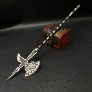 May include: A silver axe with a decorative design on the blade. The axe is attached to a long, twisted handle. The axe is resting on a small, ornate wooden box.