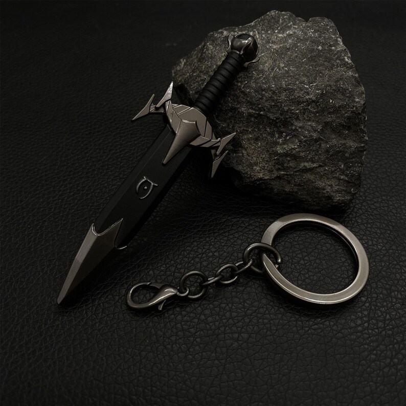 Puede incluir: Un llavero con forma de espada negra y plateada. El llavero presenta un dise&ntilde;o detallado de espada con empu&ntilde;adura y hoja negras, y detalles plateados. Incluye un llavero y un cierre.