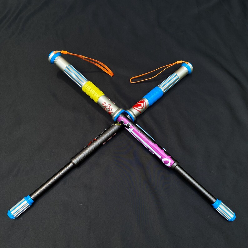 May include: Four colorful, extendable walking sticks are crossed against a black background. Each stick has a different color scheme, including blue, yellow, pink, and silver accents. They have wrist straps and are designed for outdoor activities.